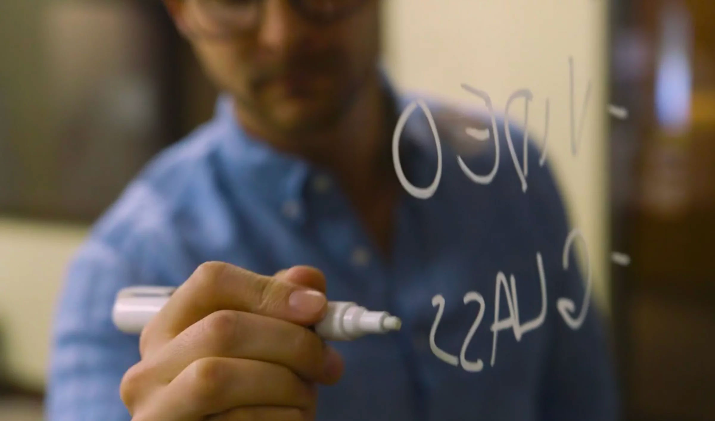 close up of hand writing on glassboard