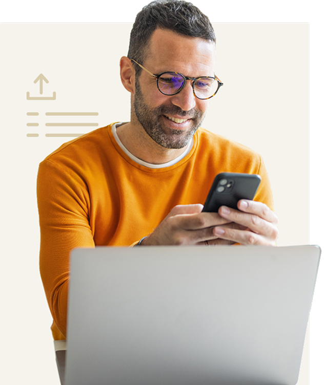 Smiling man in glasses uses smartphone at laptop
